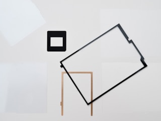 A minimalist composition features various geometric shapes arranged on a neutral background. These include a black square frame and a rectangular frame, along with a L-shaped object, all spread irregularly across the image.