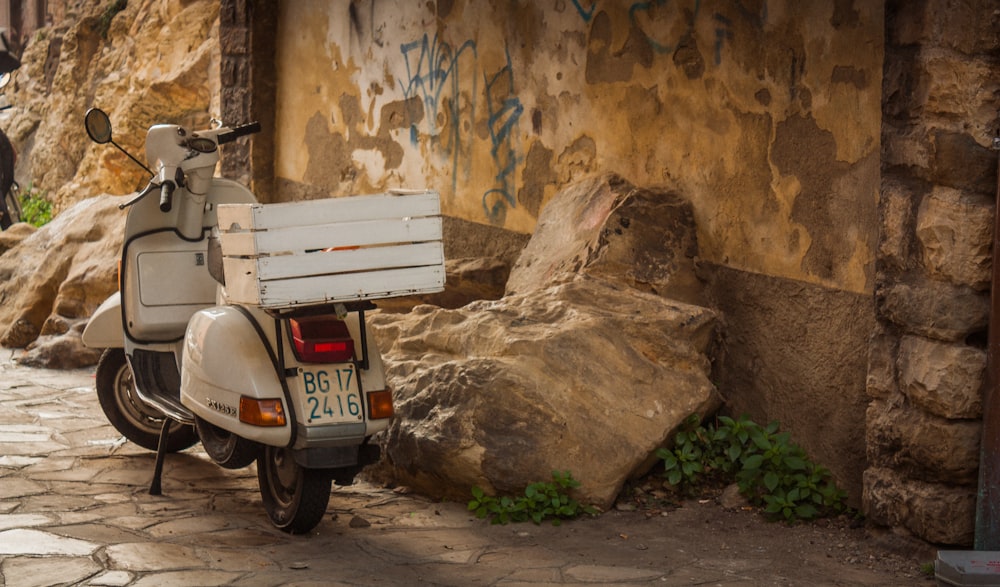 white and black motor scooter parked beside brown concrete wall