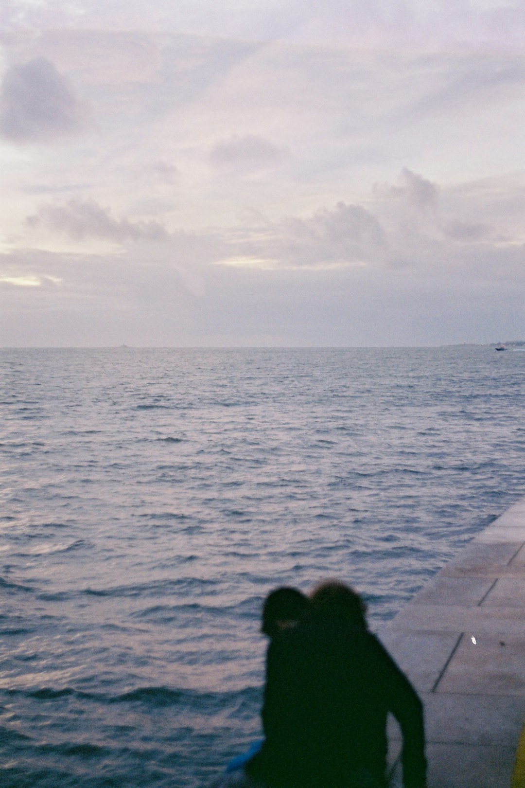 person sitting on concrete bench near sea during daytime