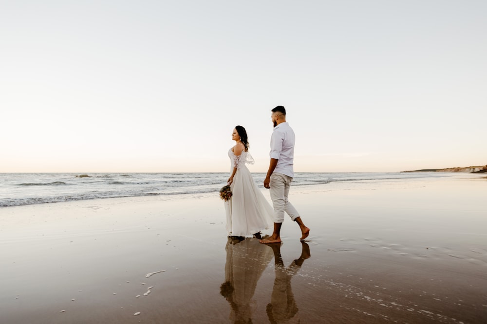 man and woman holding hands while walking on beach during daytime