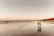 Cinematic shot of a couple walking hand-in-hand along a sandy beach at sunset.
