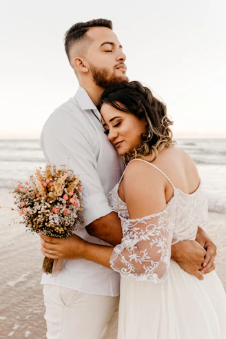 man in white suit kissing woman in white floral dress on beach during daytime