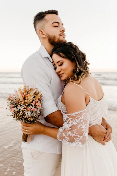 man in white suit kissing woman in white floral dress on beach during daytime