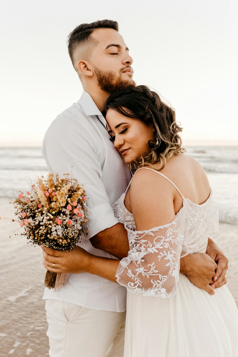 man in white suit kissing woman in white floral dress on beach during daytime