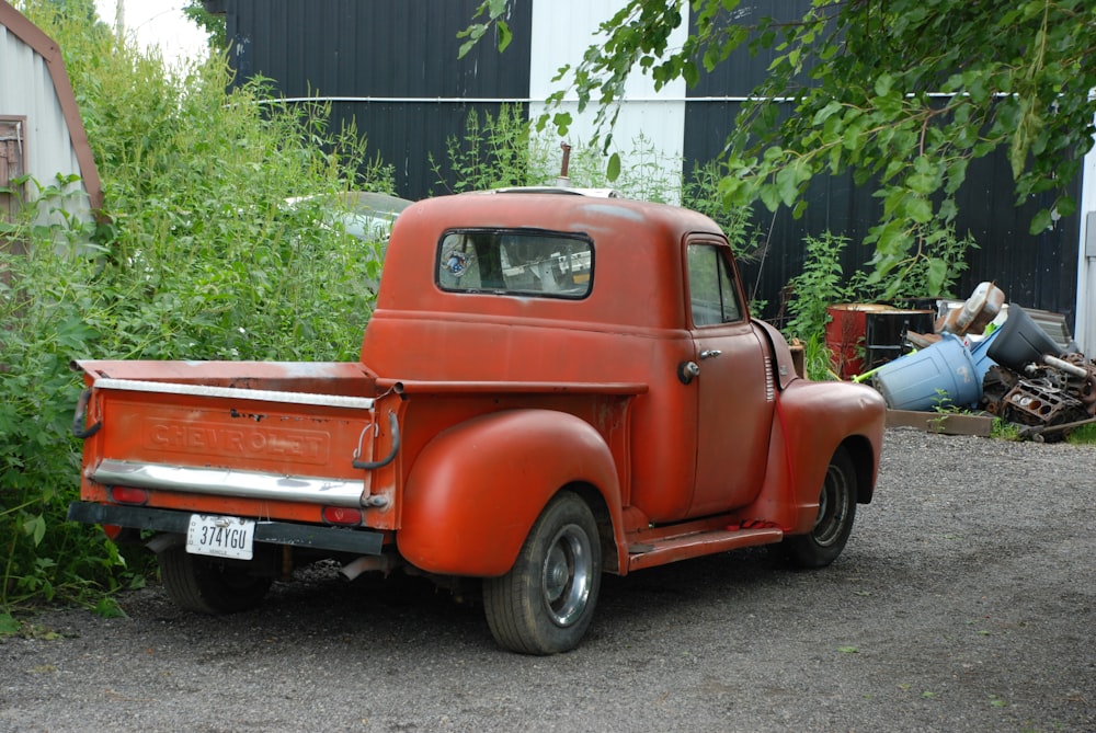 red single cab pickup truck parked near green tree during daytime