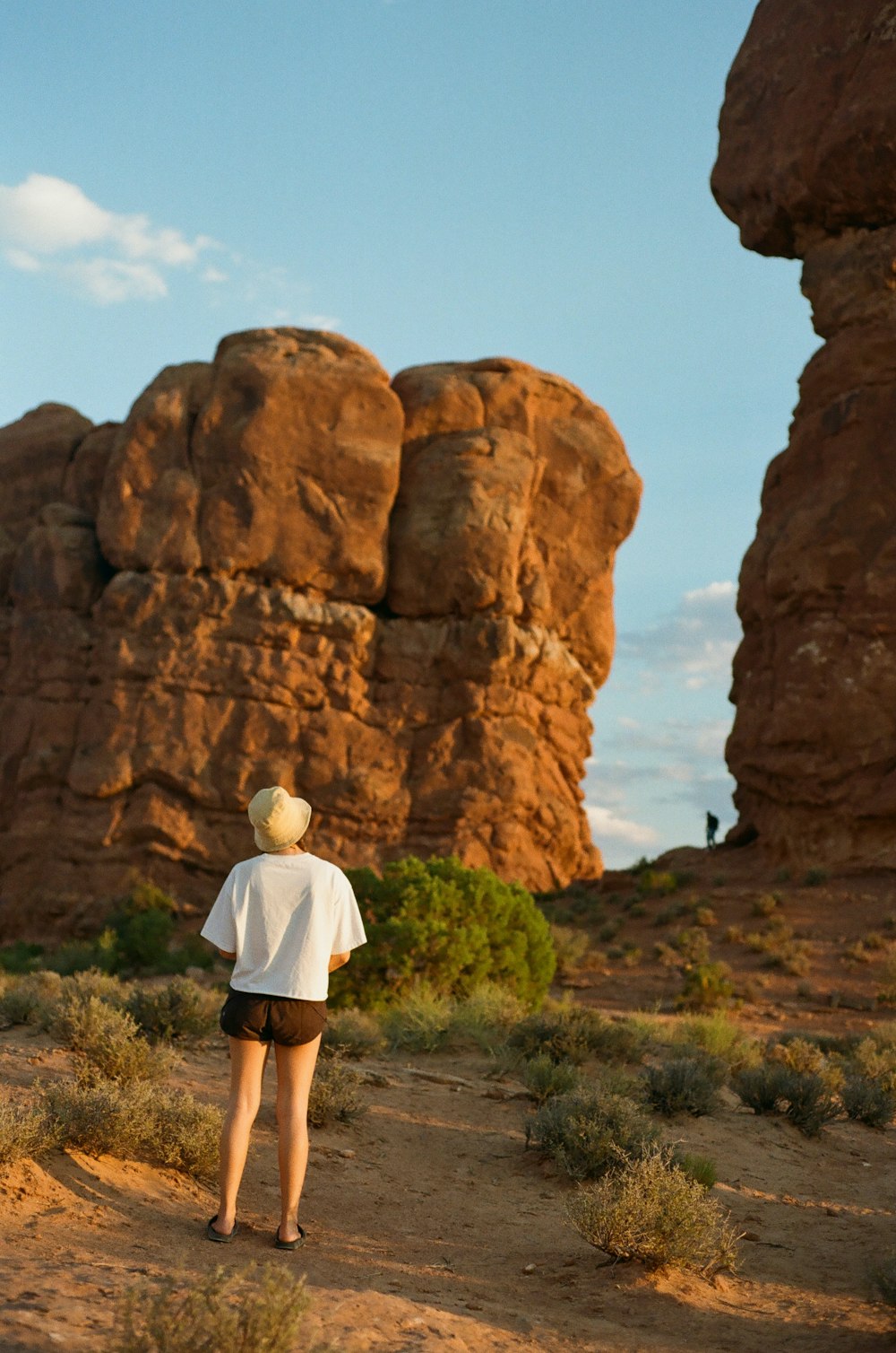 woman in white shirt and white shorts standing near brown rock formation during daytime