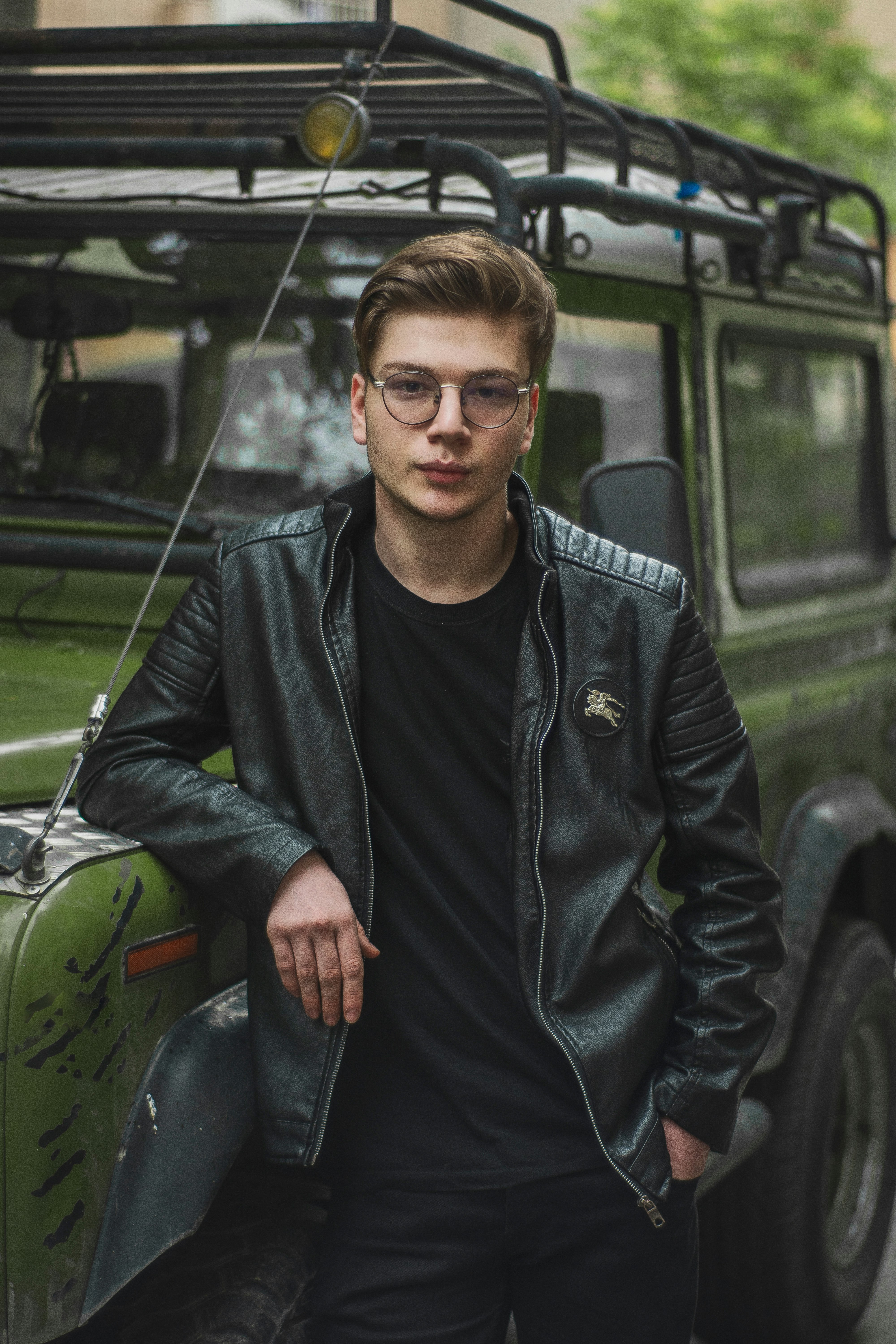 man in black leather jacket and black denim jeans sitting on green car