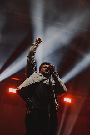 An artist passionately performing on stage with a mic, crowd cheering.