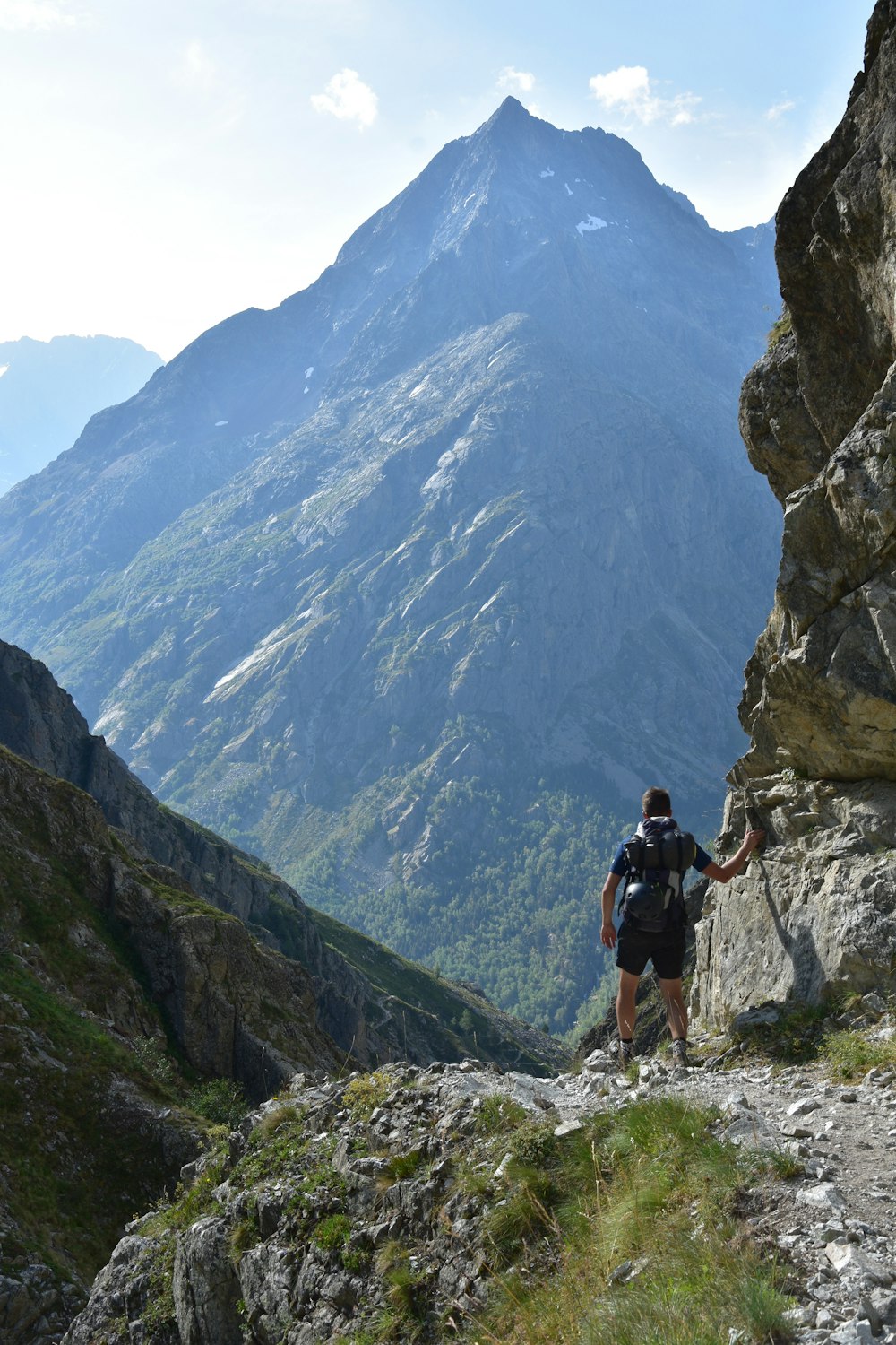 Hombre con camisa negra y pantalones cortos negros caminando en la montaña rocosa durante el día