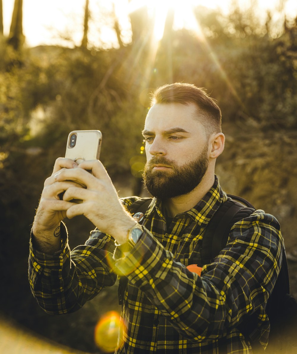 man in blue and yellow plaid dress shirt holding gold iphone 6