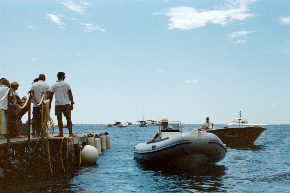 man in white t-shirt standing on brown rock near body of water during daytime