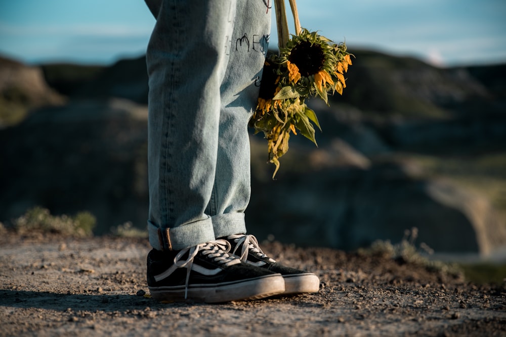 person in blue denim jeans and black and white sneakers standing on brown sand during daytime