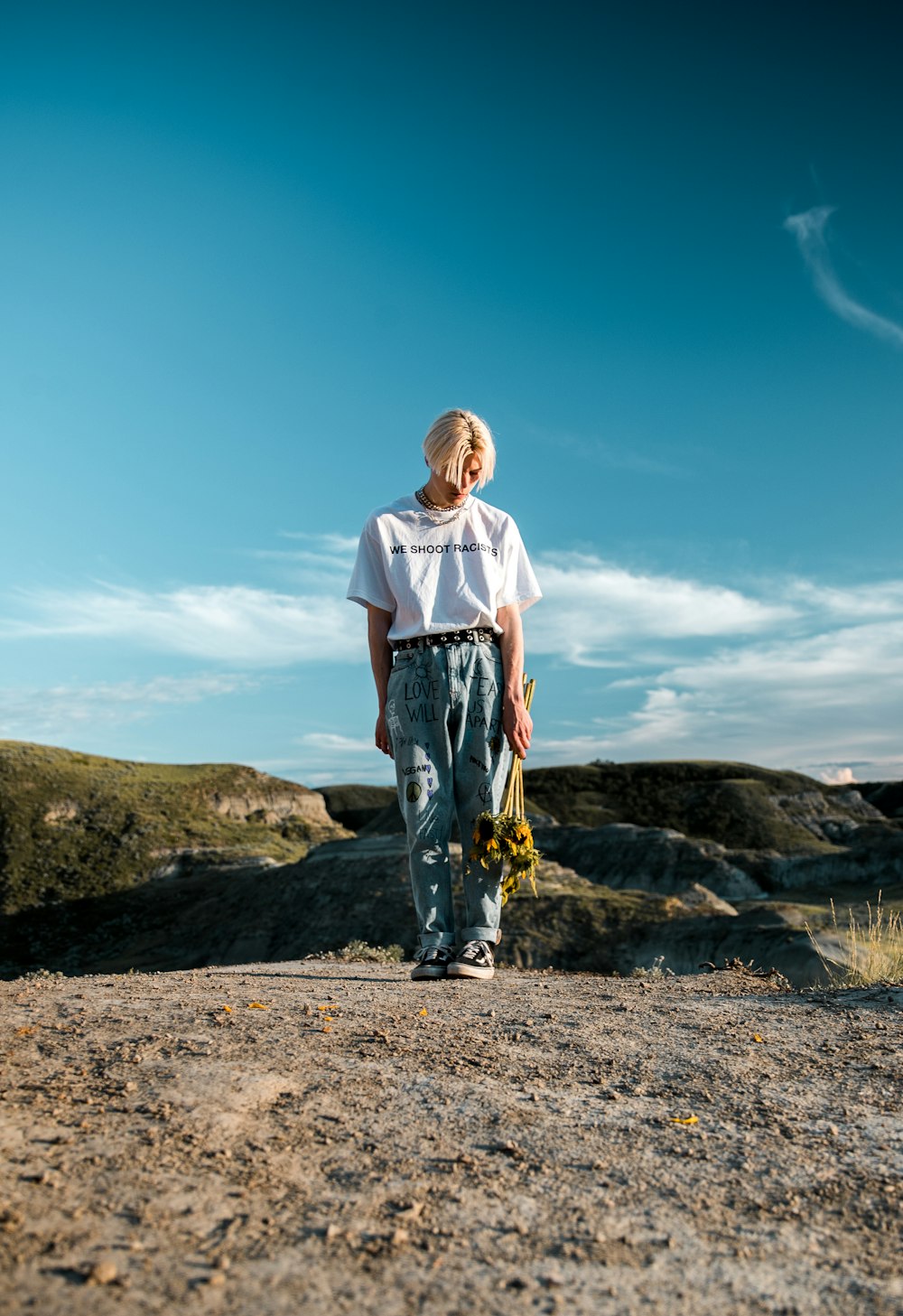 man in white t-shirt and blue denim jeans standing on brown rock during daytime