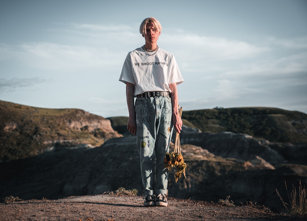 man in white crew neck t-shirt standing on brown field during daytime