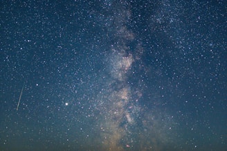 A star-filled night sky with a visible Milky Way galaxy stretching across the horizon. Countless stars are scattered throughout the dark expanse with a shooting star visible in the frame.