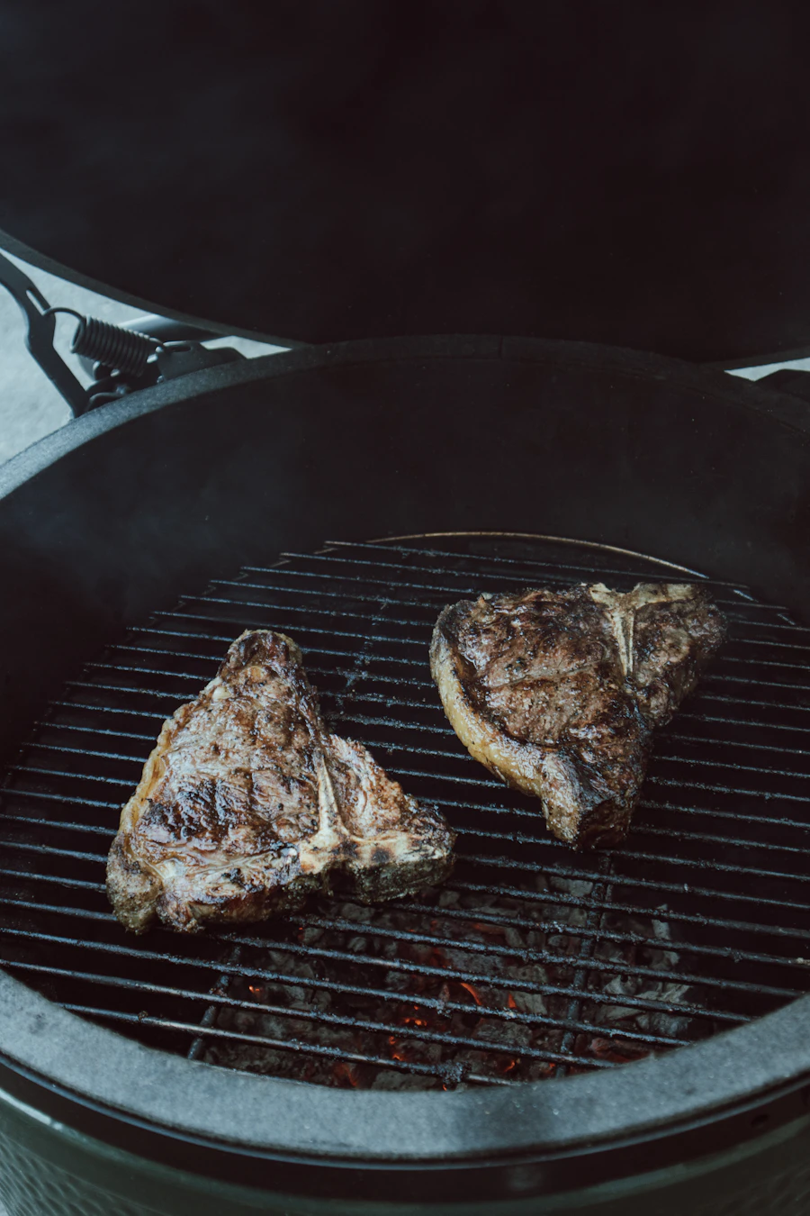 Two large porterhouse steaks grilling over glowing coals