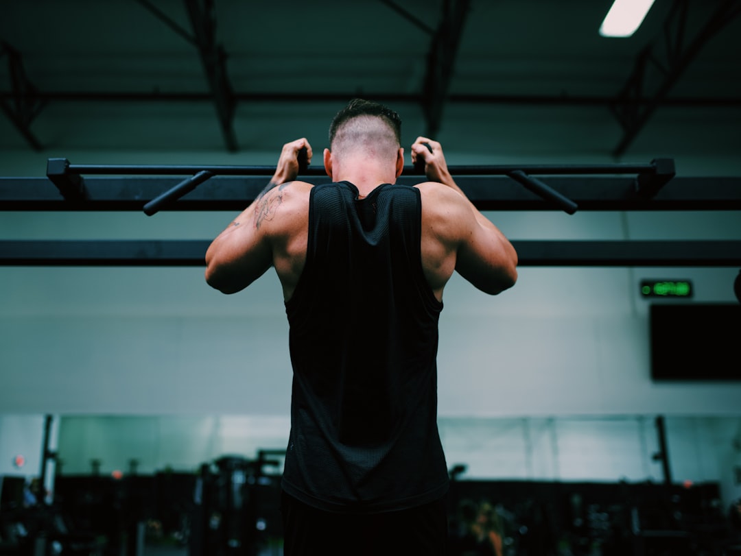 man in black tank top raising his hands, A picture of a man doing a pull up in the gym