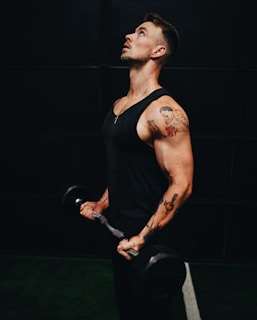 man in black tank top holding black dumbbell