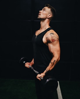 man in black tank top holding black dumbbell