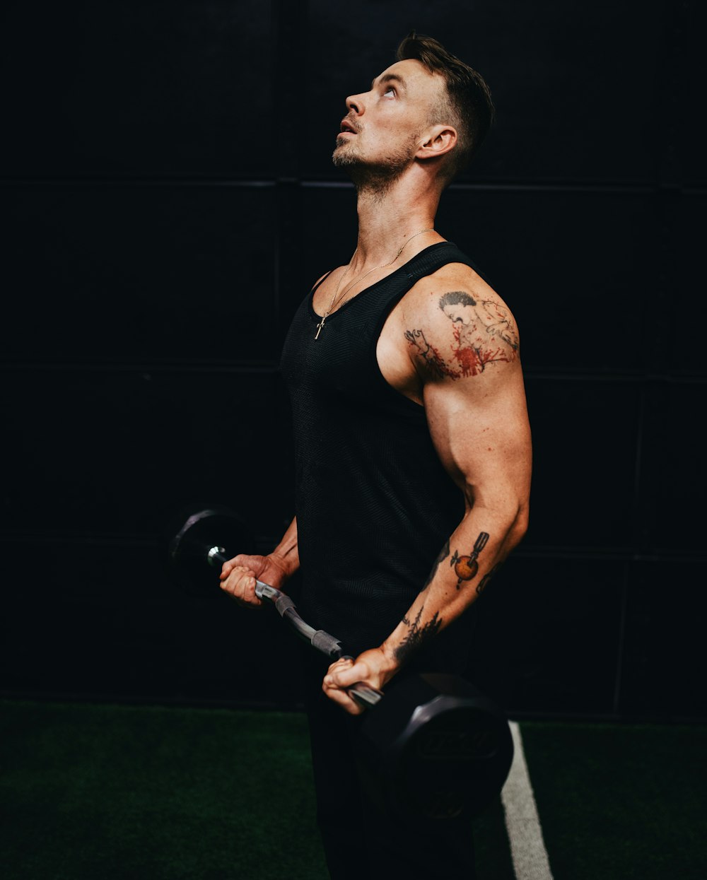 man in black tank top holding black dumbbell