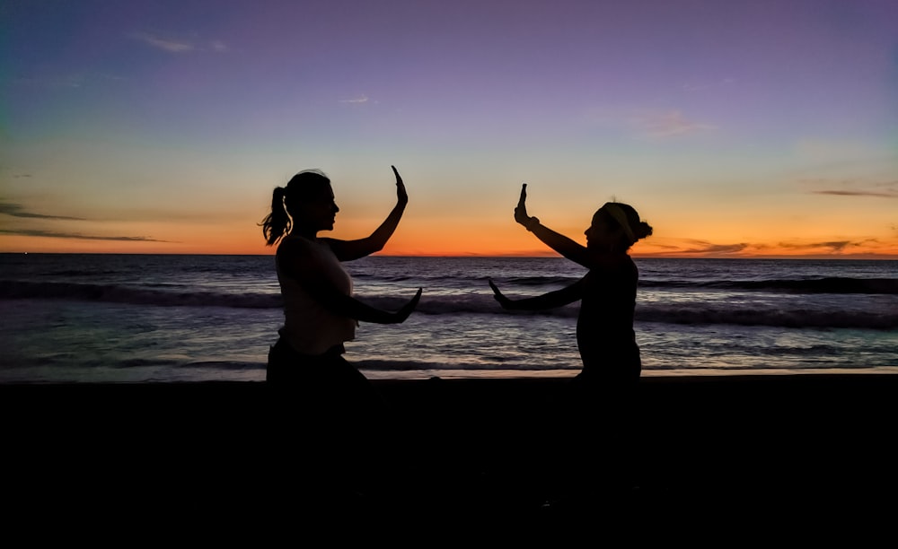 silhouette of 2 women standing on beach during sunset