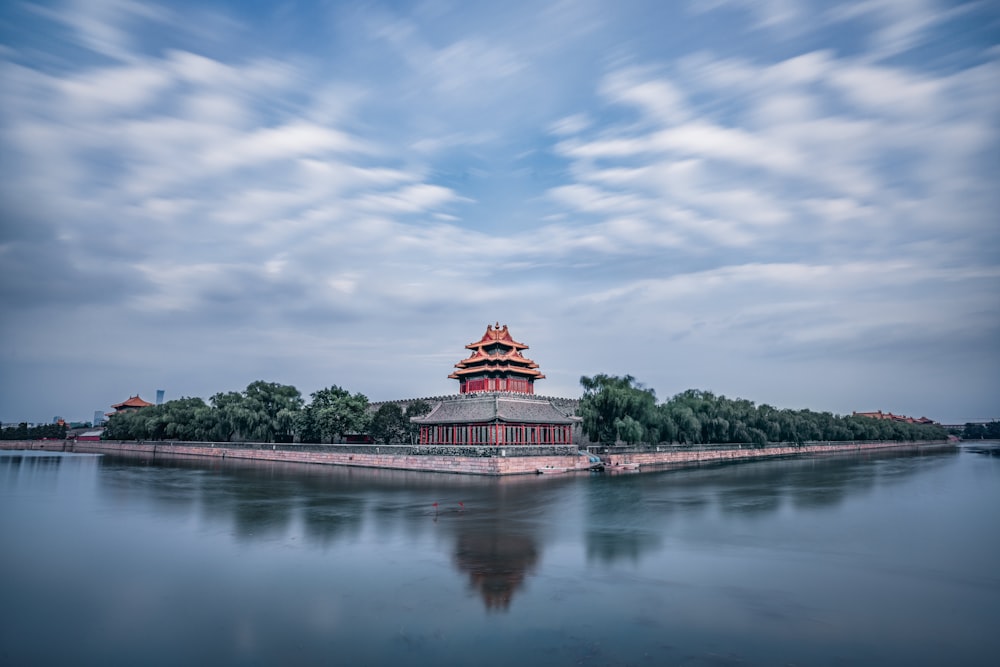 red and white temple near green trees and lake under blue sky and white clouds during