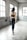 A person with long dark hair is wearing a black sports outfit, consisting of a sports bra and leggings. They are standing in a spacious, industrial-style room with tall windows that let in natural light. The walls are gray and slightly worn, adding a rustic charm to the setting.
