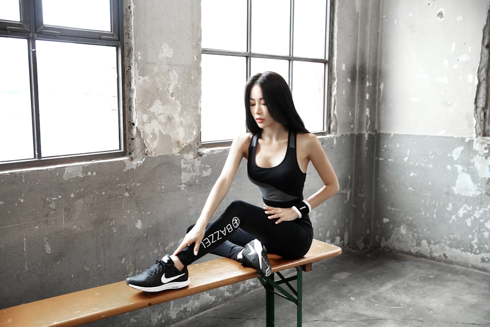 woman in black tank top and black pants sitting on brown wooden bench