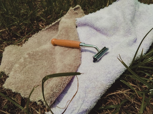 A sleek razor resting on a wooden bathroom counter next to a small potted plant and a neatly folded towel.
