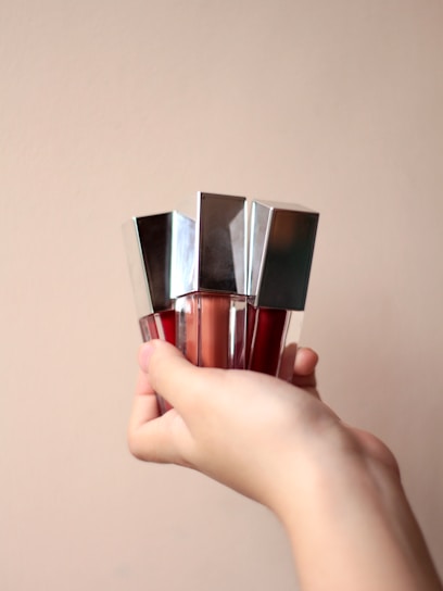 A close-up of diverse hands holding different shades of liquid foundation bottles against a soft pastel background.