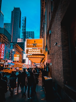 A vibrant New York City street scene with a young drama student holding a script, surrounded by iconic theater marquees and digital AI graphics blending into the background.