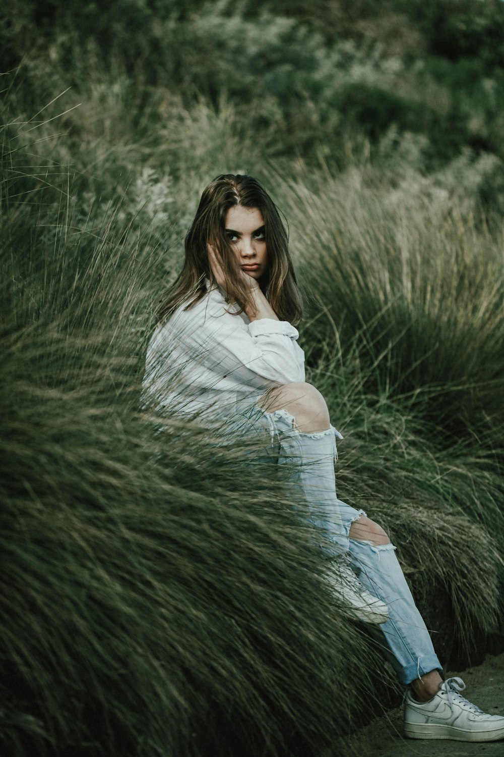 woman in white long sleeve shirt and blue denim jeans sitting on green grass field during