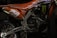 A close-up view of a motorcycle's engine and rear section painted in orange and adorned with various decals. The number '259' is prominently displayed in white. The intricate details of the metallic components and the rugged tire are visible, along with brand logos such as Monster Energy.