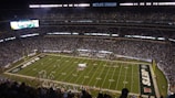 A packed high school football stadium under bright lights with fans cheering.