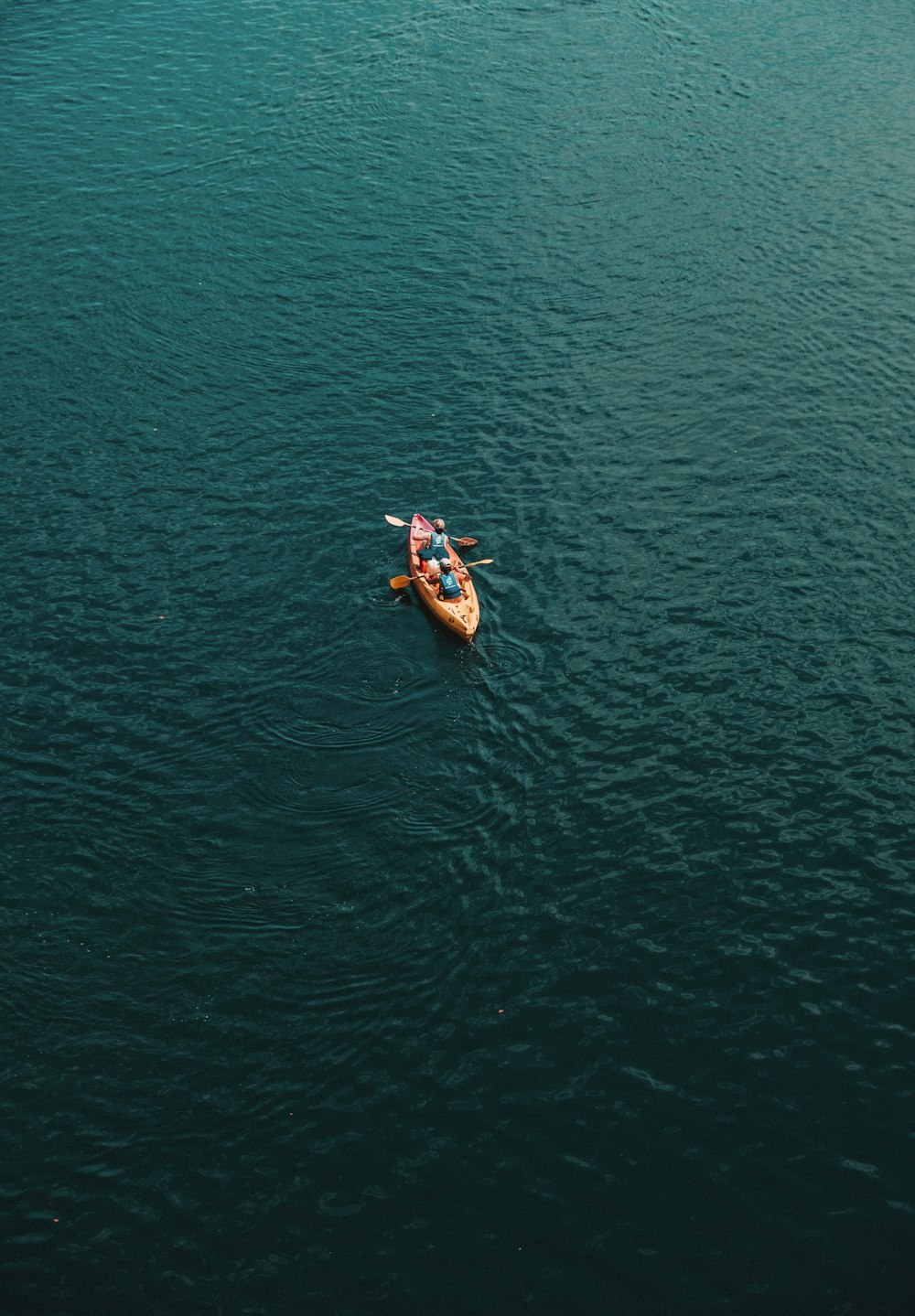 2 person riding on orange kayak on green sea during daytime