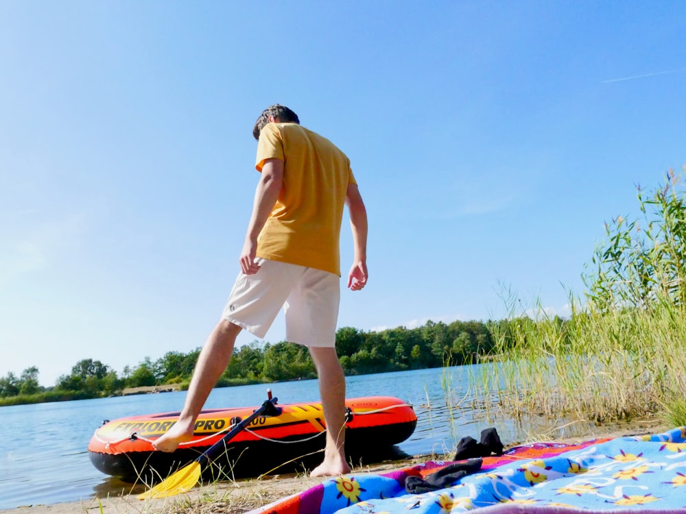 man in yellow polo shirt and white shorts standing on red and blue kayak during daytime