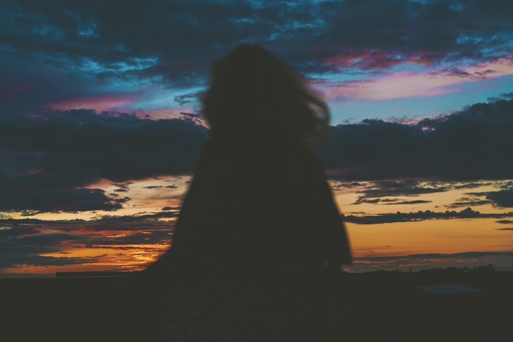 silhouette of woman sitting on beach during sunset