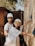 Two individuals wearing hard hats and protective eyewear are involved in construction work, assembling a wooden structure. They appear focused and collaborative, dressed casually with one of them smiling at the camera.