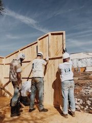 2 men in white hard hat standing on brown wooden fence during daytime