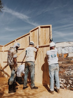 2 men in white hard hat standing on brown wooden fence during daytime