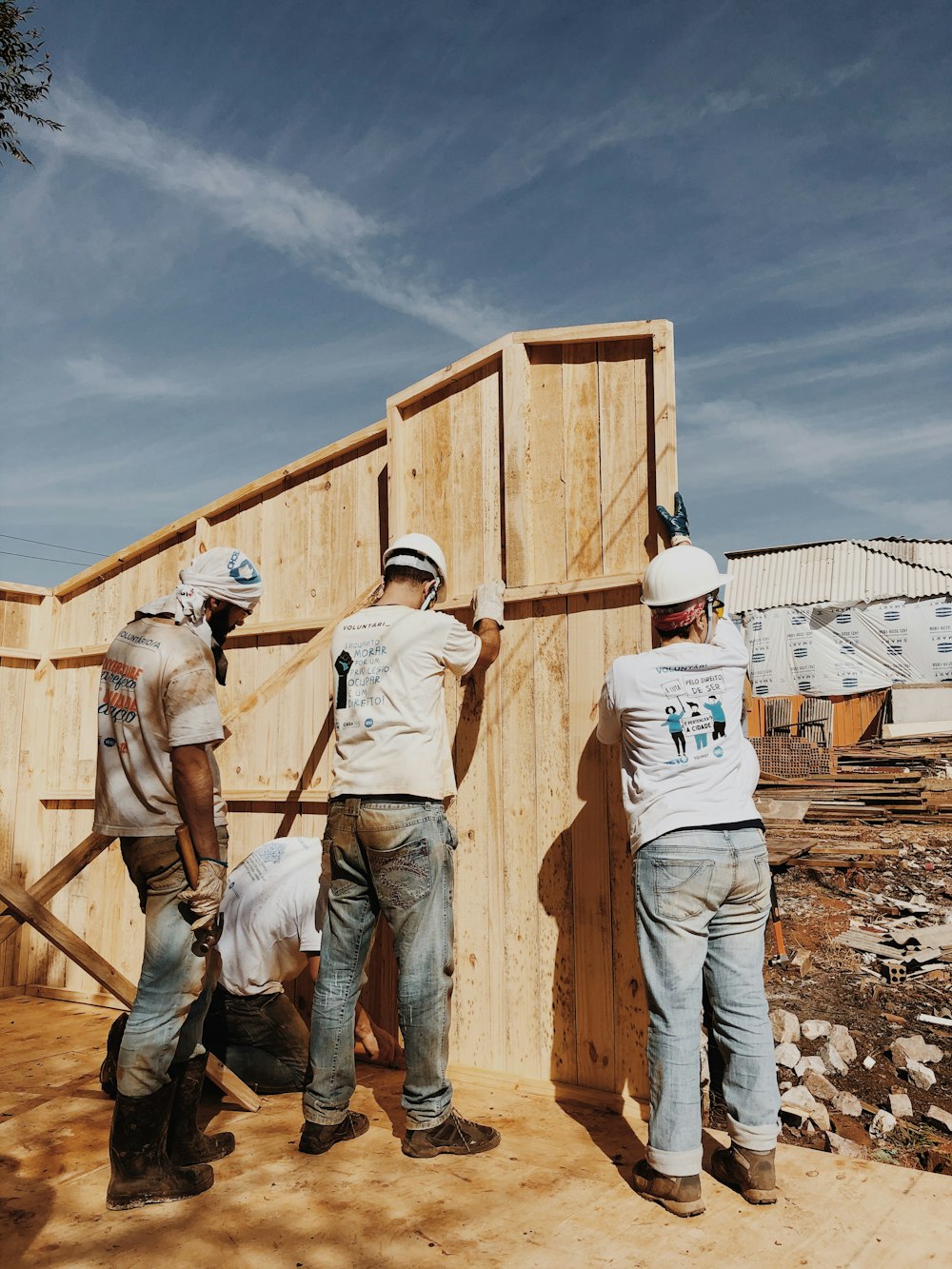 2 men in white hard hat standing on brown wooden fence during daytime