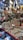 A market stall displays a variety of shiny metal items, including bowls, cups, and decorative pieces, with intricate designs. The items are made from materials like brass and copper. Decorative hangings and vibrant items are suspended above the stall, adding color and texture.