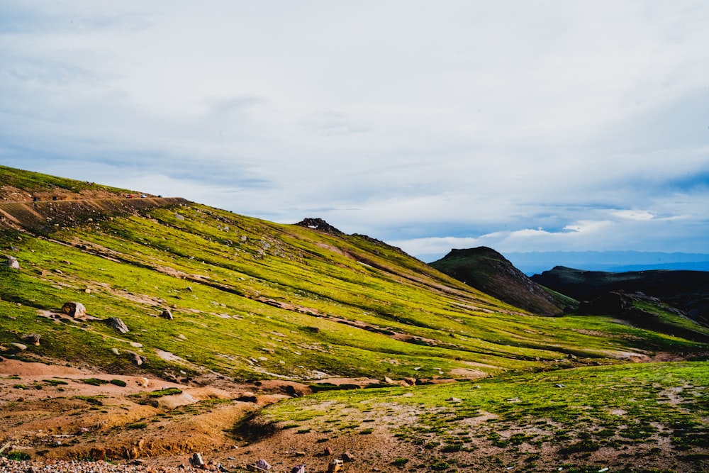 green grass field on hill under white clouds during daytime