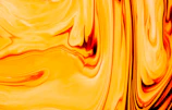 Bright yellow and orange hair dye blending together in a swirl pattern inside a mixing cup.
