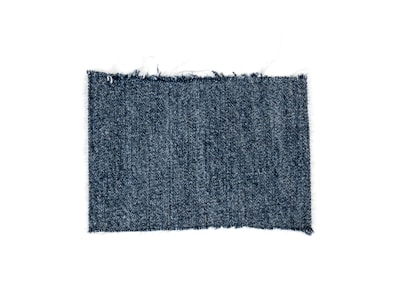 A rectangular piece of blue denim fabric with a textured, woven pattern and slightly frayed edges.