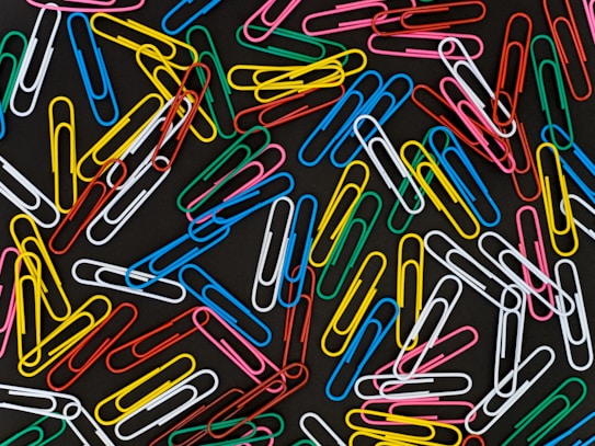 A scattered arrangement of multicolored paperclips on a dark background creates a vibrant and chaotic pattern.