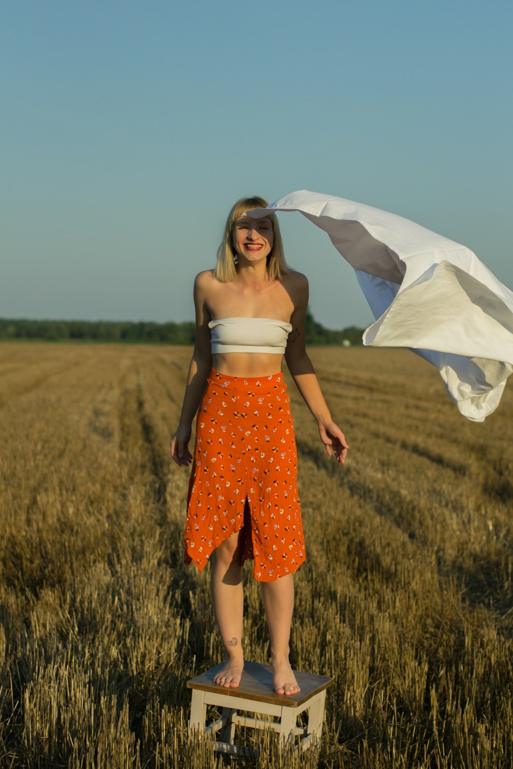 woman in white and red floral spaghetti strap dress standing on green grass field during daytime