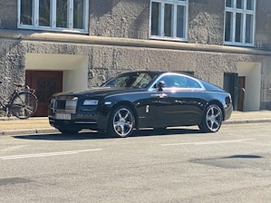 A sleek car with a driver waiting beside it ready for rental service.