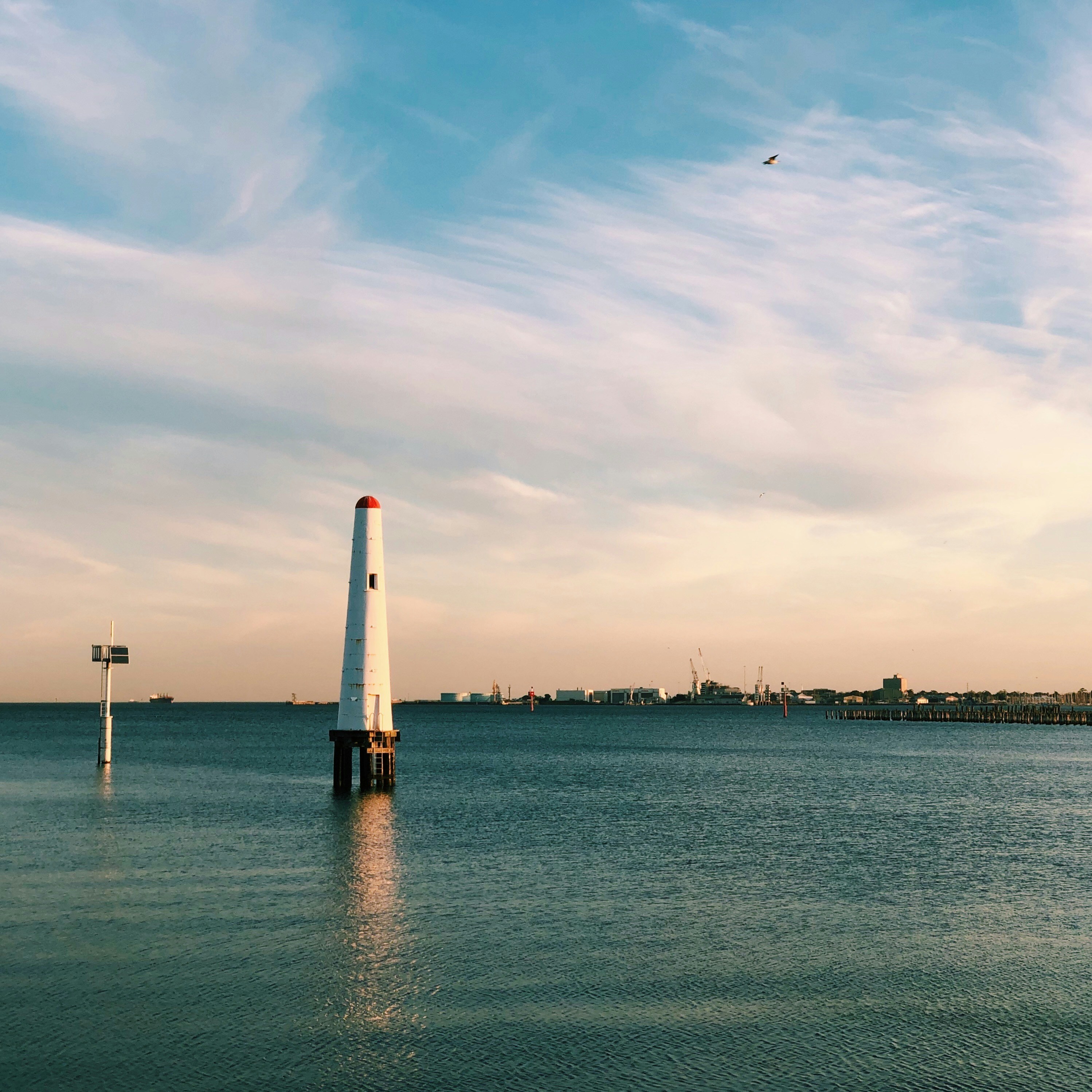 white and orange lighthouse on sea under white clouds during daytime