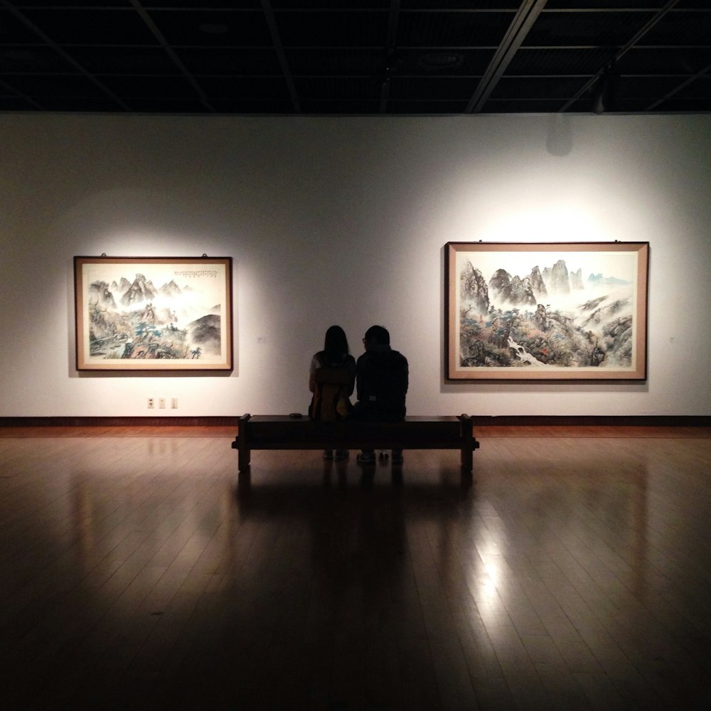 2 women sitting on bench near tree painting